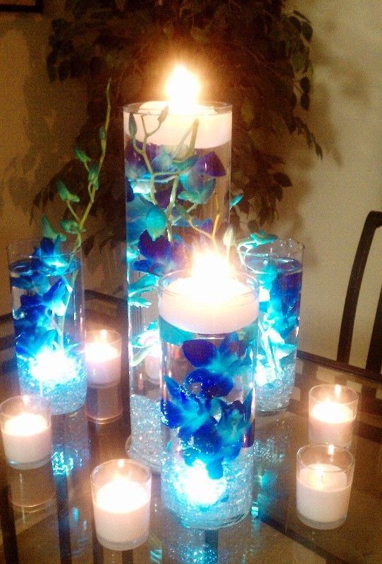 blue orchids submerged in vases filled with water and floating candles on the to