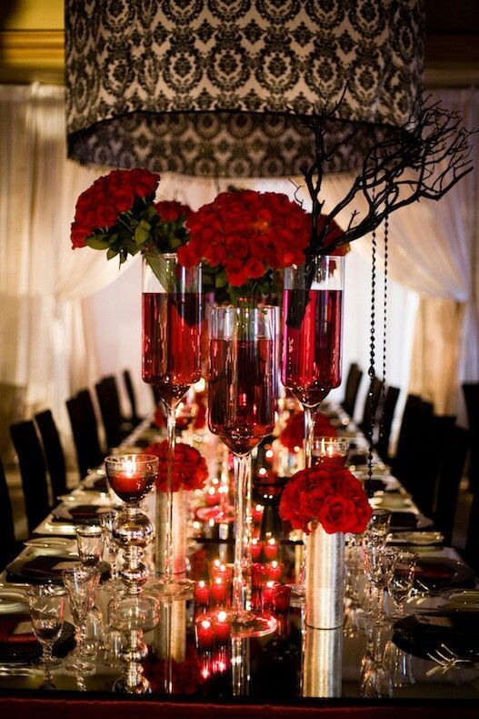 Table setting for a red, black, and white wedding with roses and damask print.