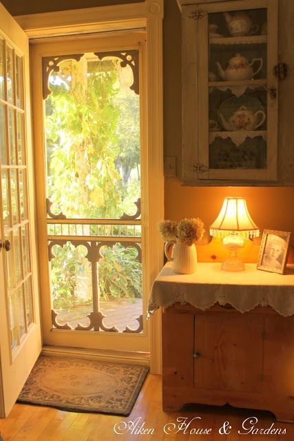 I love everything about this small scene: Lovely screen door – I want my screen doors that decorative! Warm colors, love the cloth laying on the cabinet top,