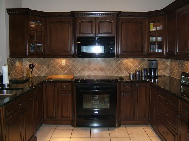 Brown kitchen cabinets with dark countertop and lighter colored tile backsplash and floors.