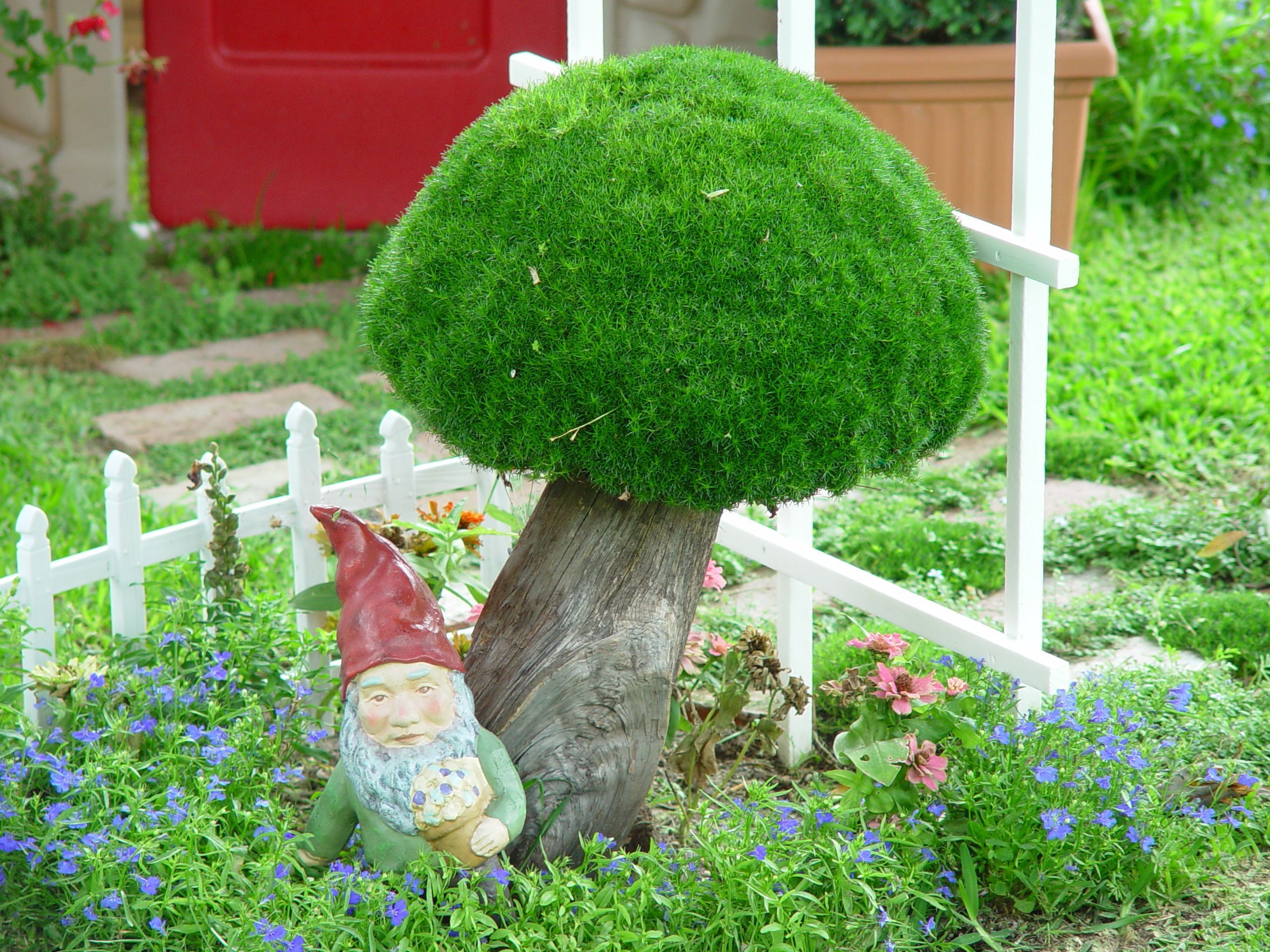 So cute! A moss basket makes a great mushroom accent in the garden!  The overturned moss basket sits on a old piece of wood