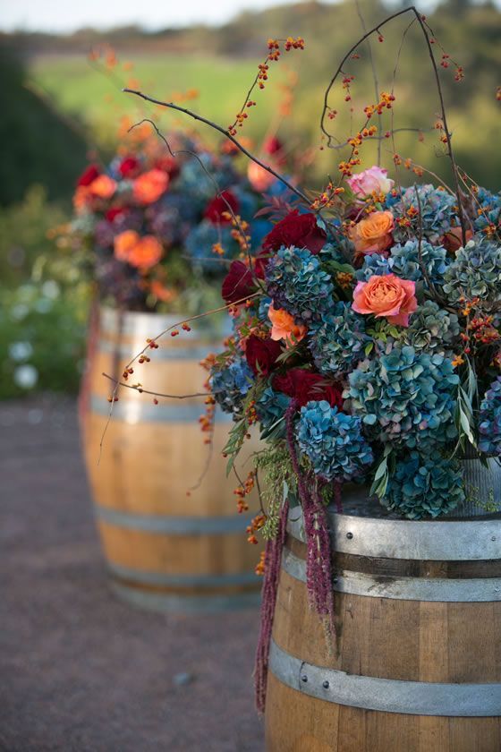 Blue hydrangea and branches atop wine barrels are the perfect winery wedding flower arrangement. Petalworks.