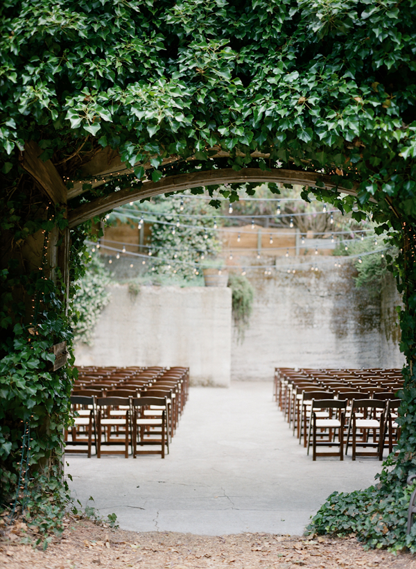 secret garden ceremony space | dark wood folding chairs with cafe string lights overhead, tucked into a grove of greenery. | Sand