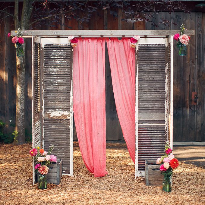 A rustic #wedding altar made of weathered shutters and gauzy pink fabric, complete with colorful flowers, created by Barbs